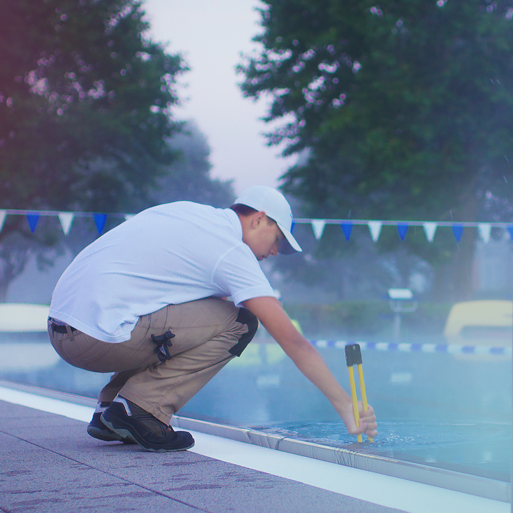 Ein Mann kontrolliert de Wasserqualität eines Schwimmbeckens im Freien
