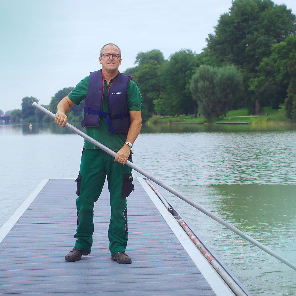 Ein Mitarbeiter der Stadt Münster steht auf dem Aasee und kümmert sich mit einem Stab um die Wasserqualität dessen.