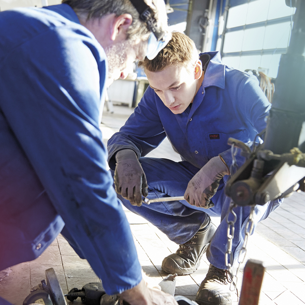 Ein auszubildender Mechatroniker wird von seinem Ausbilder bei der Reparatur eines Fahrzeugs angelernt.