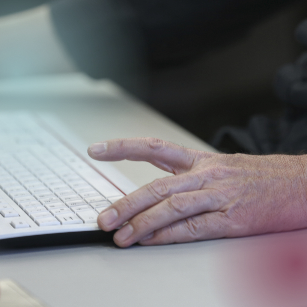 Eine Hand liegt aufgestützt neben einer Computertastatur und ist kurz davor, mit dem tippen zu beginnen.