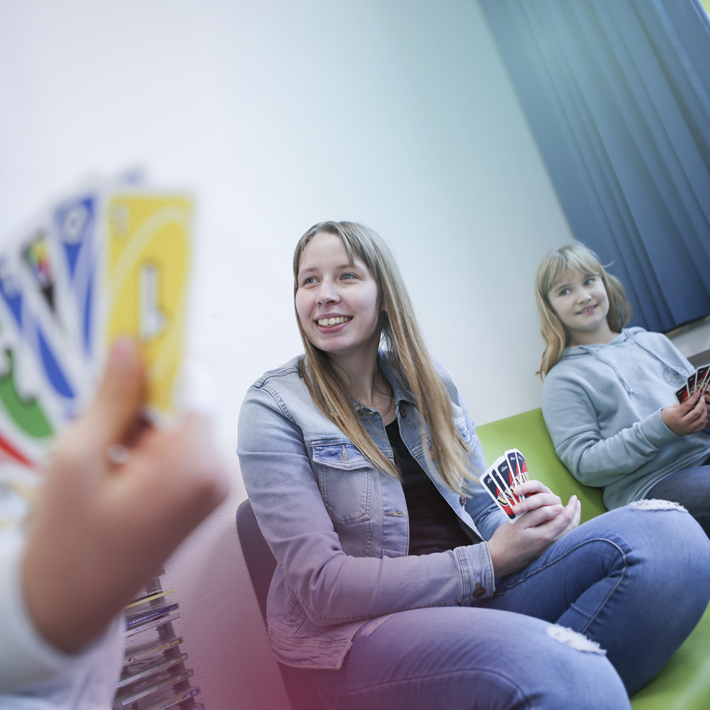 Eine Erzieherin im offenen Ganztag, einer Grundschule, spielt mit zwei Kindern das Spiel Uno.