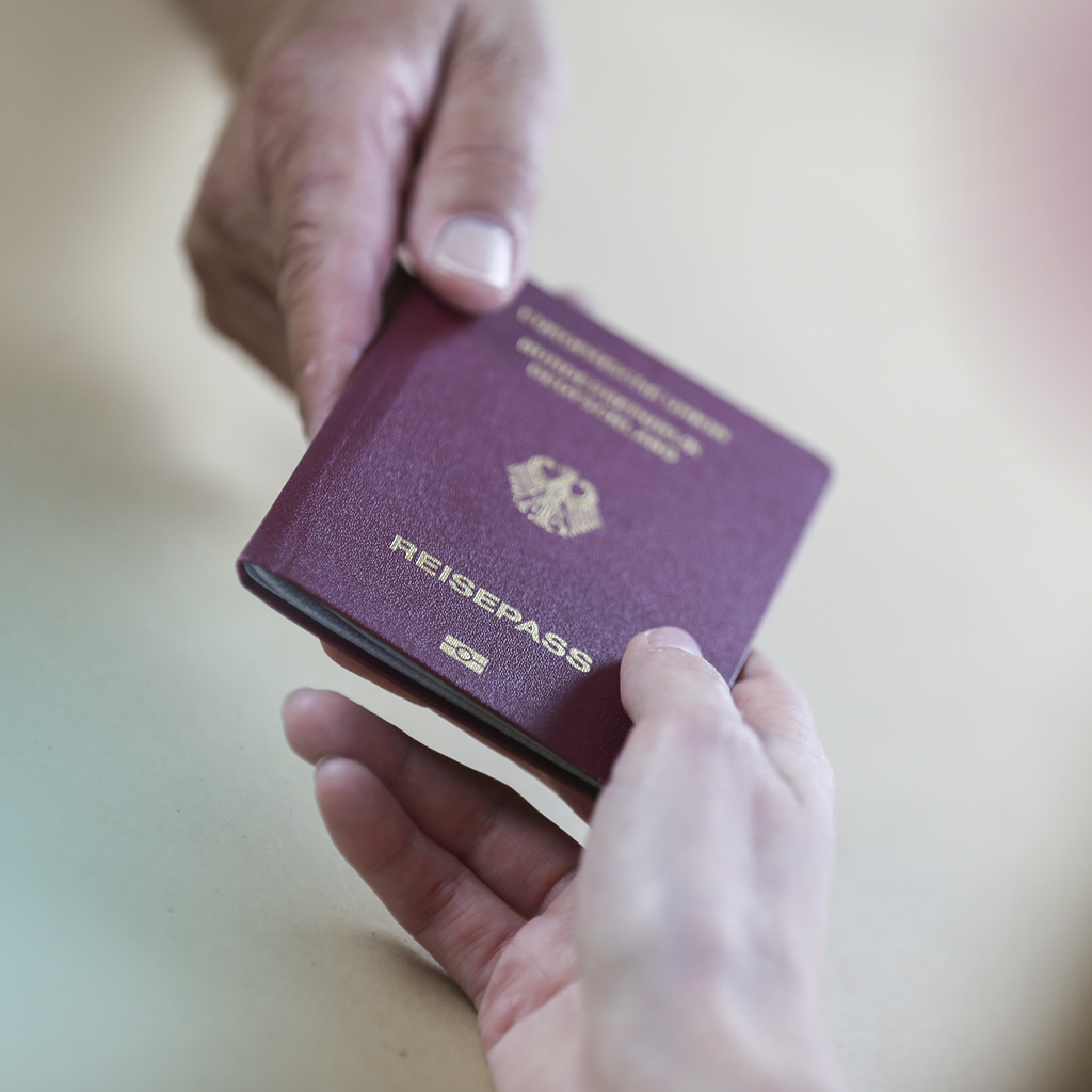 Eine weibliche Hand übergibt einer männlichen Hand einen neuen Reisepass.