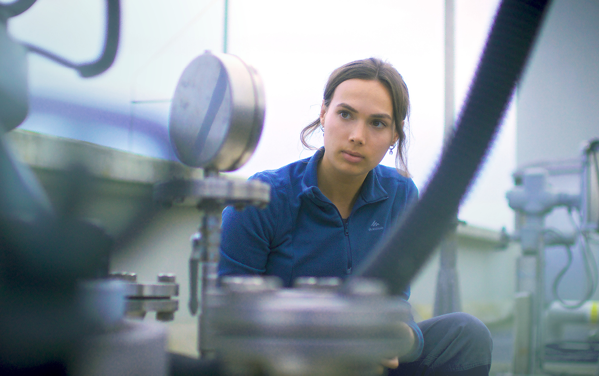 Eine junge Frau arbeitet als Fachkraft für Abwassertechnik, steht vor einem Gerät, welches den Wasserdruck misst und wertet die Ergebnisse aus.