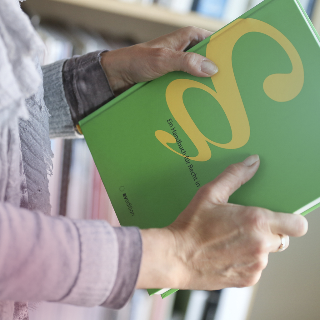 Eine Frau hält ein grünes Buch mit einem gelben Logo zum Thema Recht in beiden Händen.