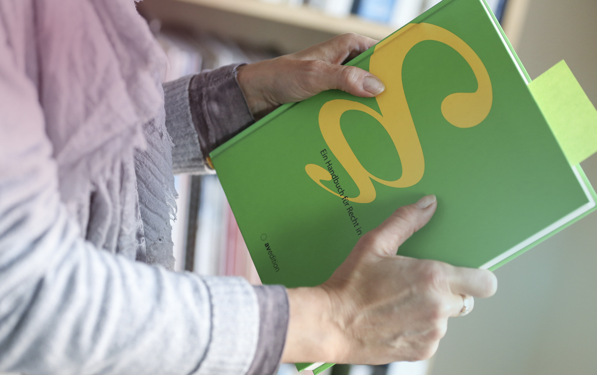 Eine Frau hält ein grünes Buch mit einem gelben Logo zum Thema Recht in beiden Händen.