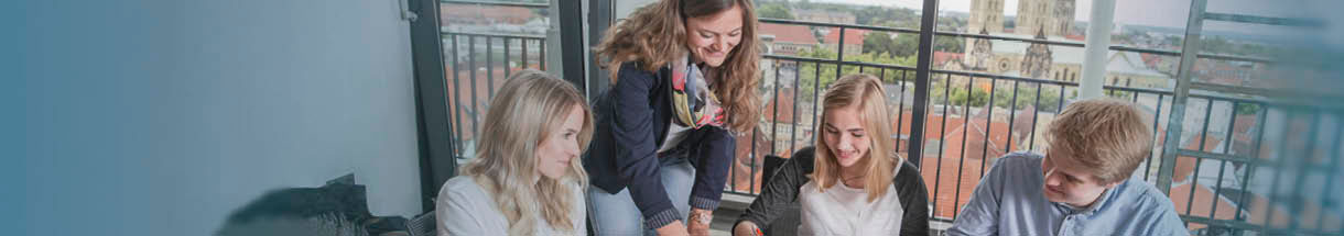 Header Stadt Münster – Vier junge Menschen arbeiten gemeinsam an einem Projekt, blaue Glasflaschen im Vordergrund