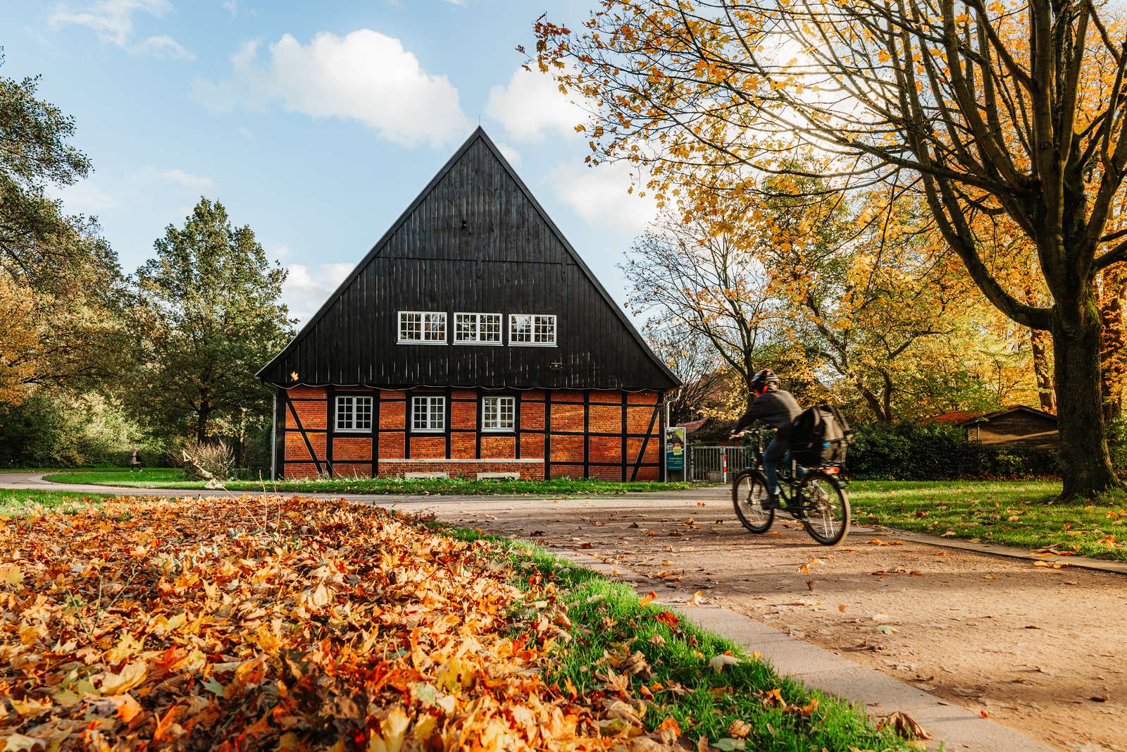 Jemand fährt in herbstlicher Umgebung mit dem Fahrrad auf einem Weg am Stadtteilhaus "Fachwerk" in Gievenbeck vorbei.