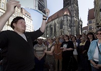 Stadtführer Patrick Gurris beim Tatort-Rundgang in Münsters Innenstadt hält er ein Blatt mit Informationen hoch, Zuschauer stehen um ihn herum