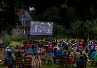 Viele Menschen sitzen auf Stühlen vor einer großen Leinwand, auf der der Film zu sehen ist.