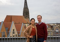 Eine junge Frau mit einem jungen Mann auf einer Dachterrasse, hinter ihnen ist der Turm der Lambertikirche zu sehen.