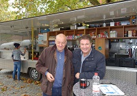 Francis Fulton-Smith und Leonard Lansink in einer Drehpause vor einem Marktwagen.