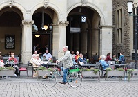 Axel Prahl fährt mit einem Fahrrad über den Prinzipalmarkt, im Hintergrund das Stadtweinhaus