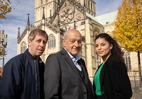 Oliver Korittke, Leonard Lansink und Patricia Meeden stehen bei Dreharbeiten auf dem Domplatz in Münster bei Sonnenschein vor dem Dom