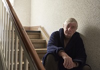 Ein alter Mann sitzt betrübt auf einer Treppe im Hausflur.