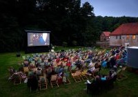 Blick über Liegestühle auf einer Wiese zu einer Leinwand auf der ein Film läuft