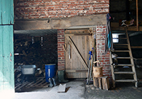 In der Stallung, links eine Schubkarre und gestapelte Holzscheite; rechts eine Treppe nach oben