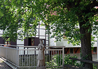 Außenansicht auf den Fachwerkbau; im Vorgergrund eine Statue unter einem Baum