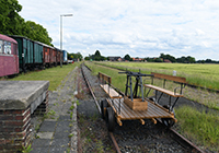 Alter Bahnhof Lette - Außenansicht, im Vordergrund eine alte, hölzerne Draisine, links alte Zugteile