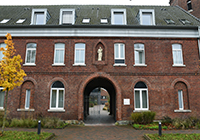 Rotes Backsteingebäude mit Torbogen und Durchfahrt auf dem Alexianer-Campus