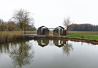 Blick über einen See auf zwei kleine Holz-Bauwerke auf dem Alexianer-Campus