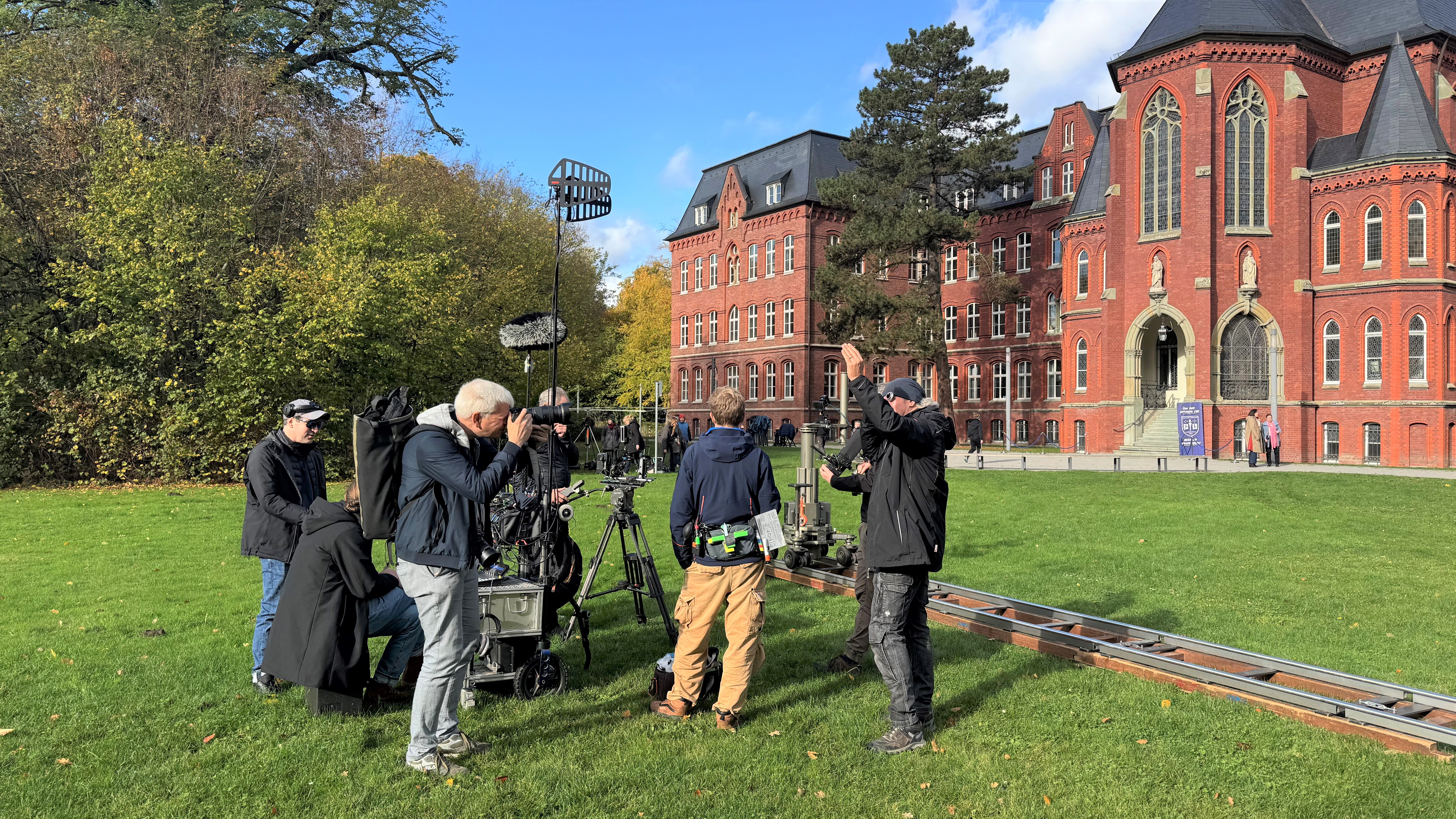 Blick auf ein Filmteam bei der Arbeit, im Hintergrund ein historischer Backsteinbau