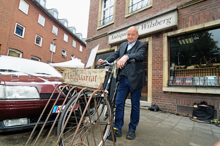 Wilsberg-Darsteller an ein Fahrrad gelehnt vor dem Antiquariat