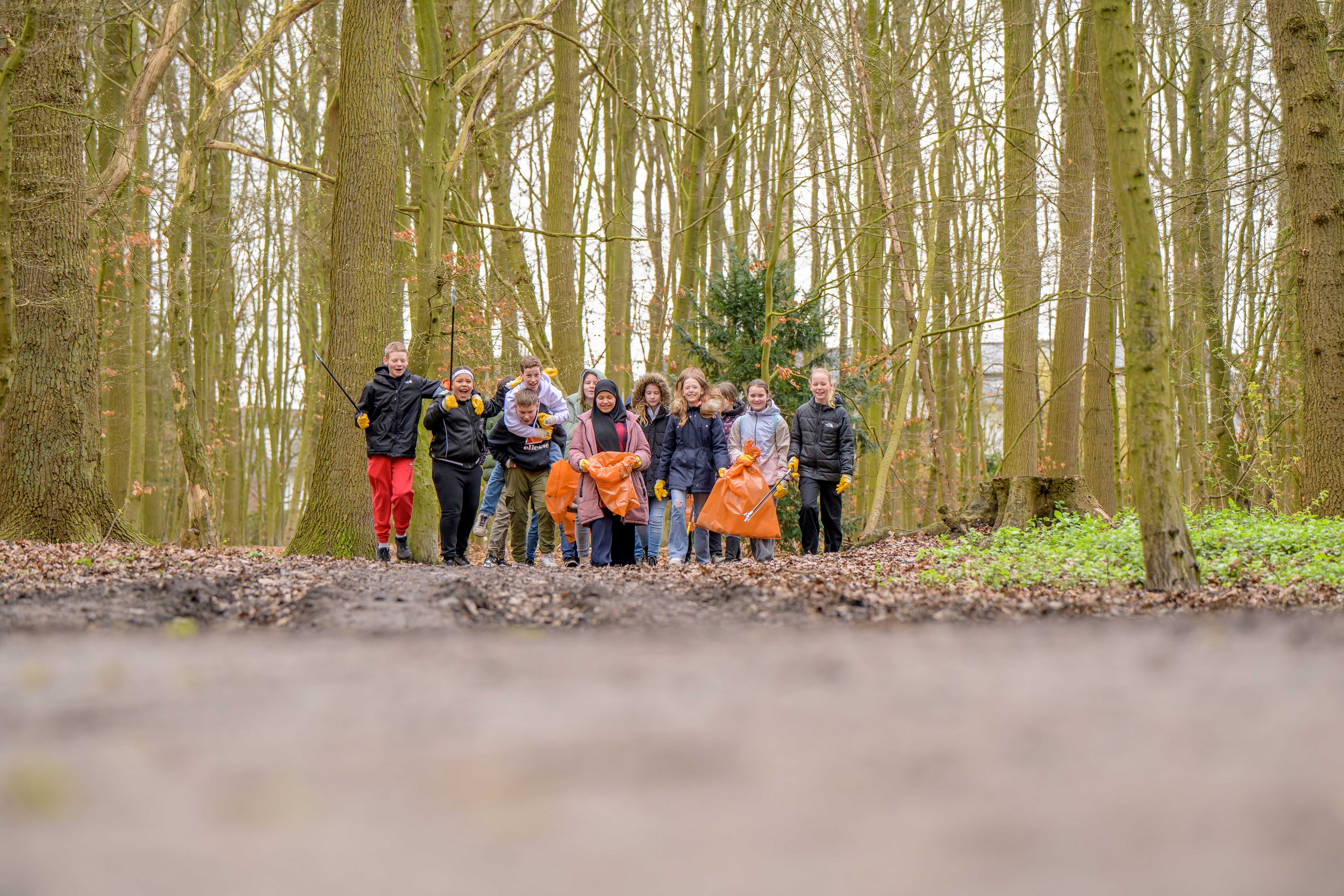 Eine Gruppe Kinder, die an der Aktion Sauberes Münster teilgenommen hat und im Wald Müll sammelt.