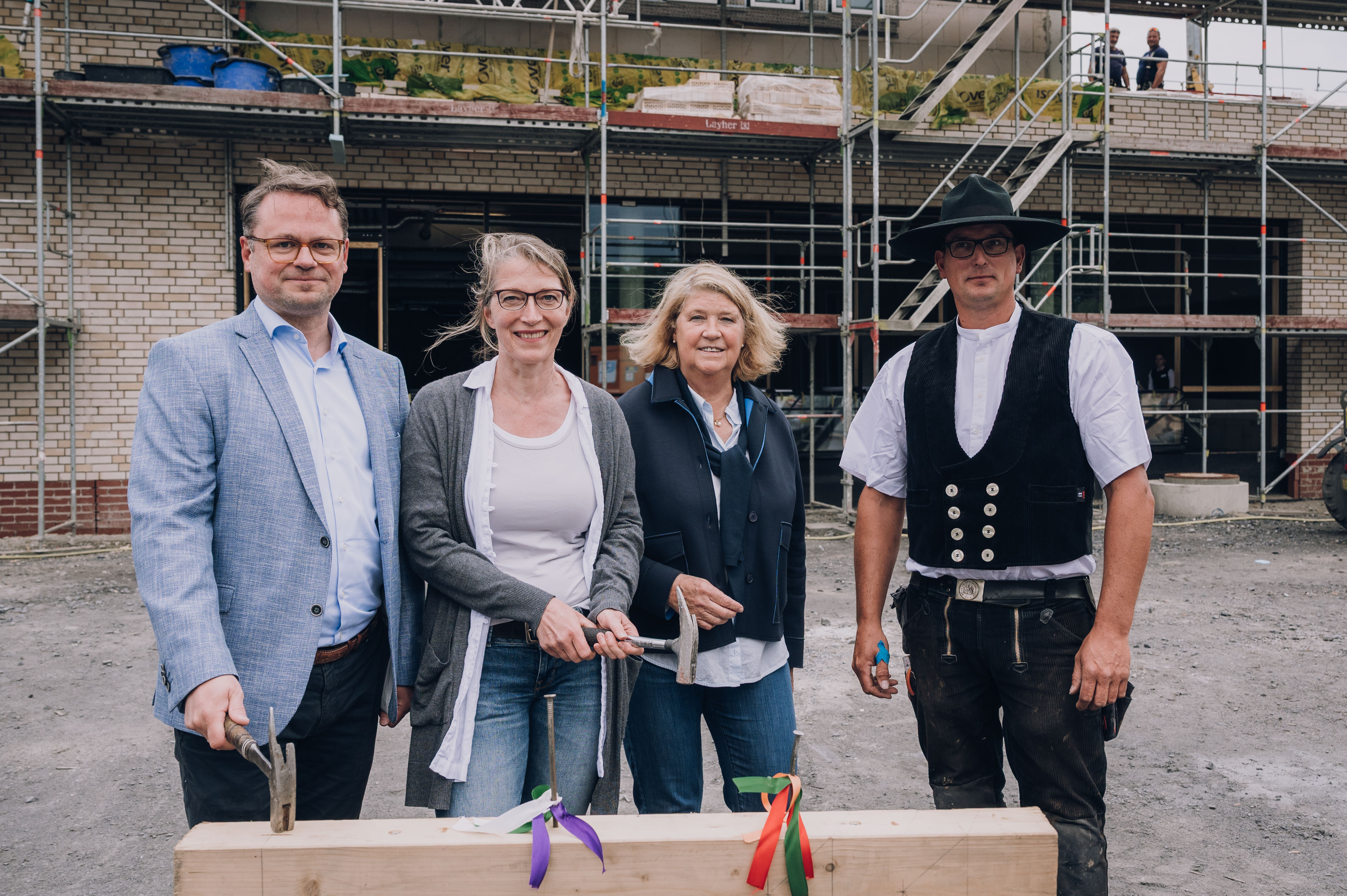 Bezirksbürgermeister Stephan Brinktrine, Bettina Haack, Projektleiterin Hanne Silies  und Zimmermann Sven Hüls schlagen beim Richtfest auf einen Nagel in einem Holzstamm ein 