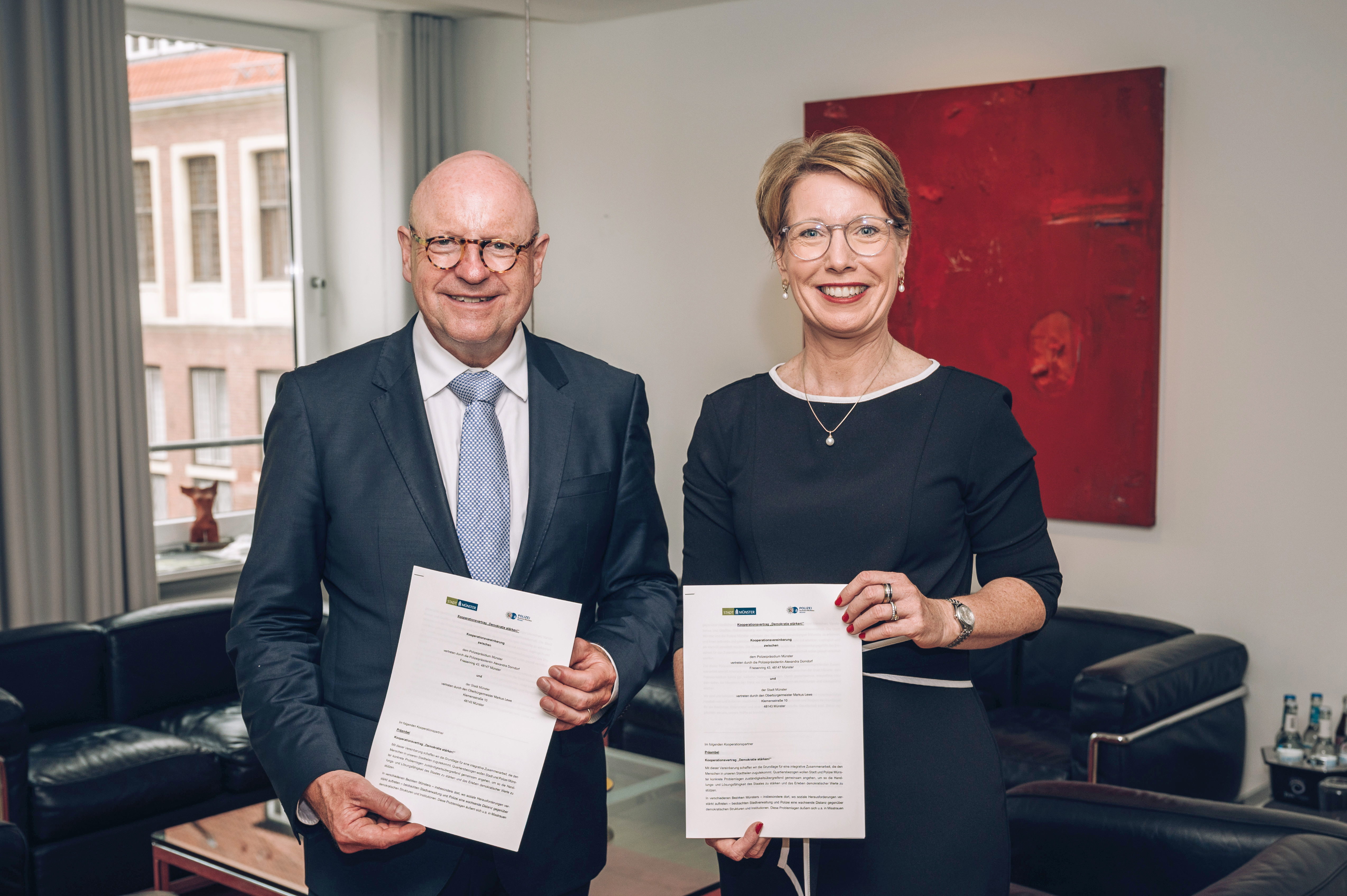 Markus Lewe und Alexandra Dorndorf stehen nebeneinander im Büro und halten jeweils das Papier mit der Kooperationsvereinbarung in den Händen.