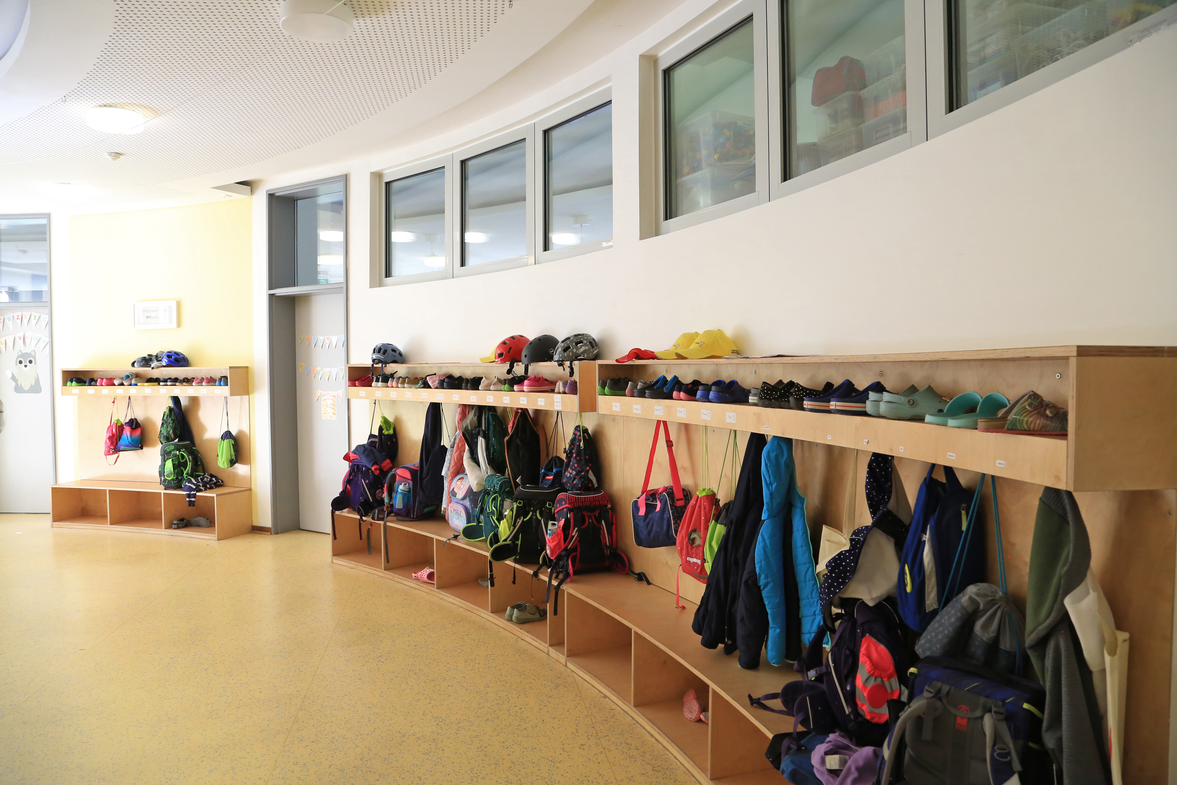 Garderobe in einer Grundschule mit mehreren Jacken und Rucksäcken von Grundschulkindern 