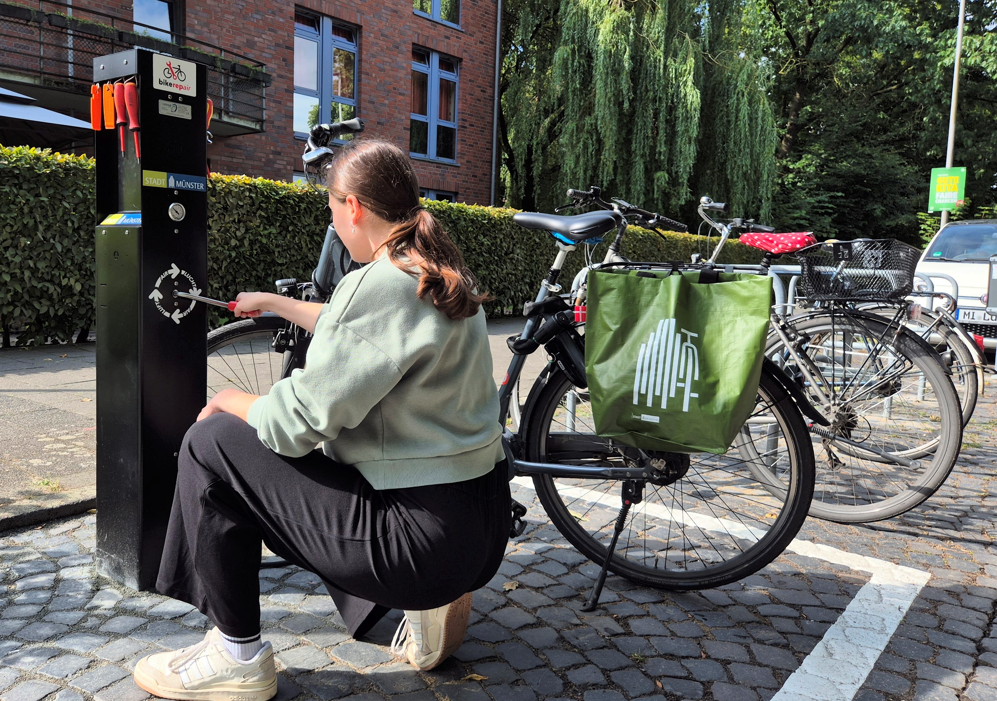 Junge Frau werkelt an einer Radservicestation auf höhe des Jugendgästehauses am Aasee an der Bismarck-Allee, im Hintergrund steht ihr Fahrrad