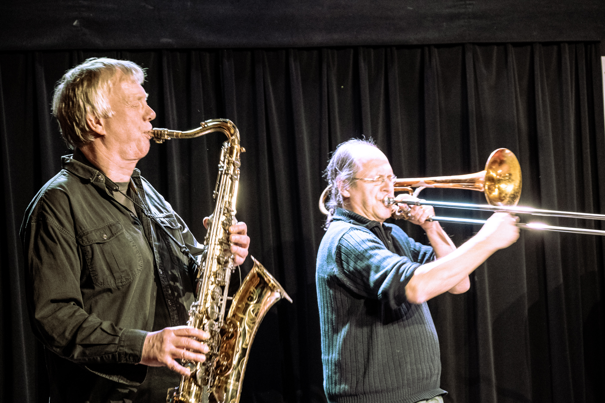 Zwei Männer auf einer Bühne, einer spielt Saxofon, der andere Trompete