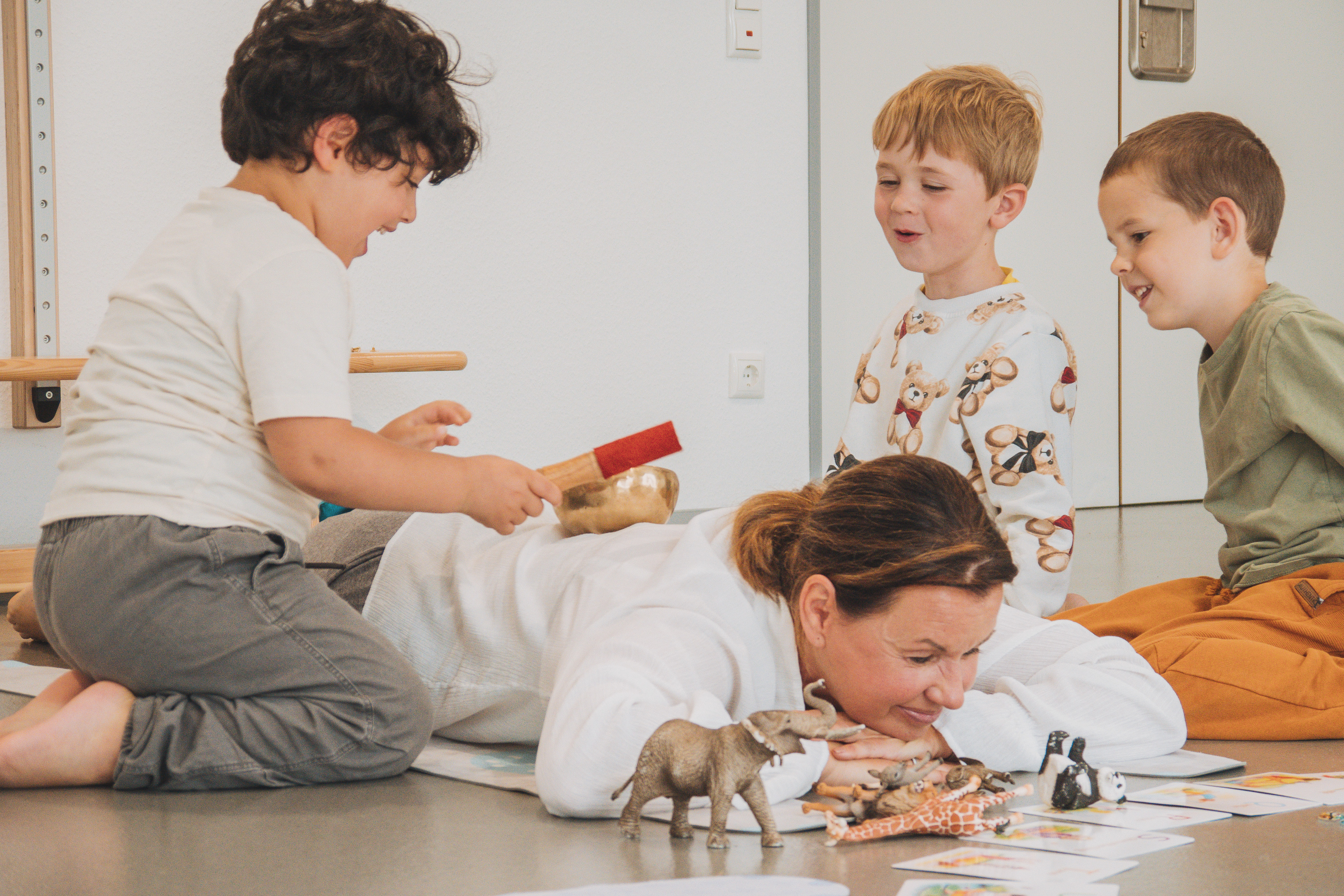 Eine auf dem Boden liegende Erzieherin und darum drei Kinder