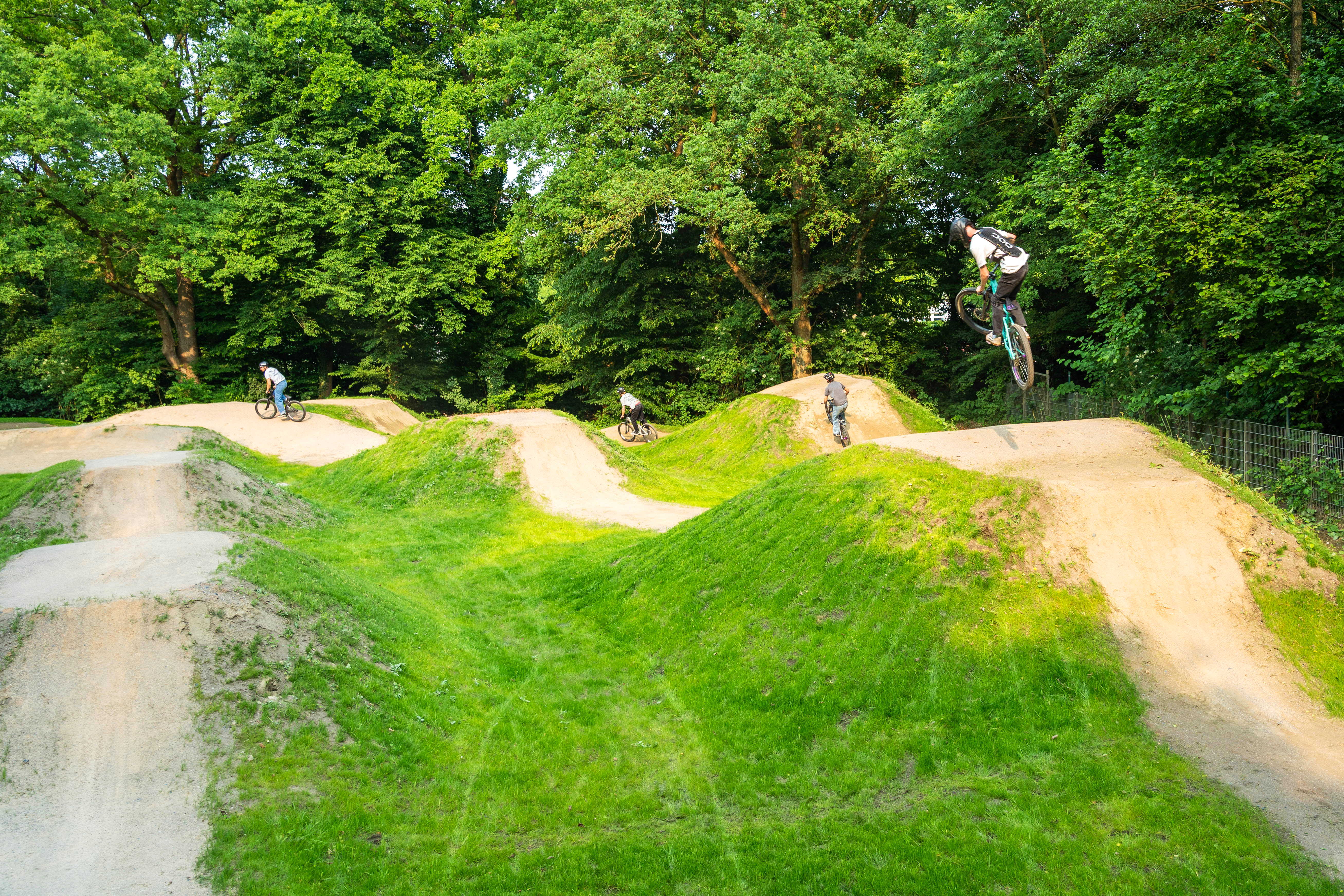 Drei Jugendliche fahren und springen mit ihren Rädern über die Dirtbike-Anlage in Berg Fidel