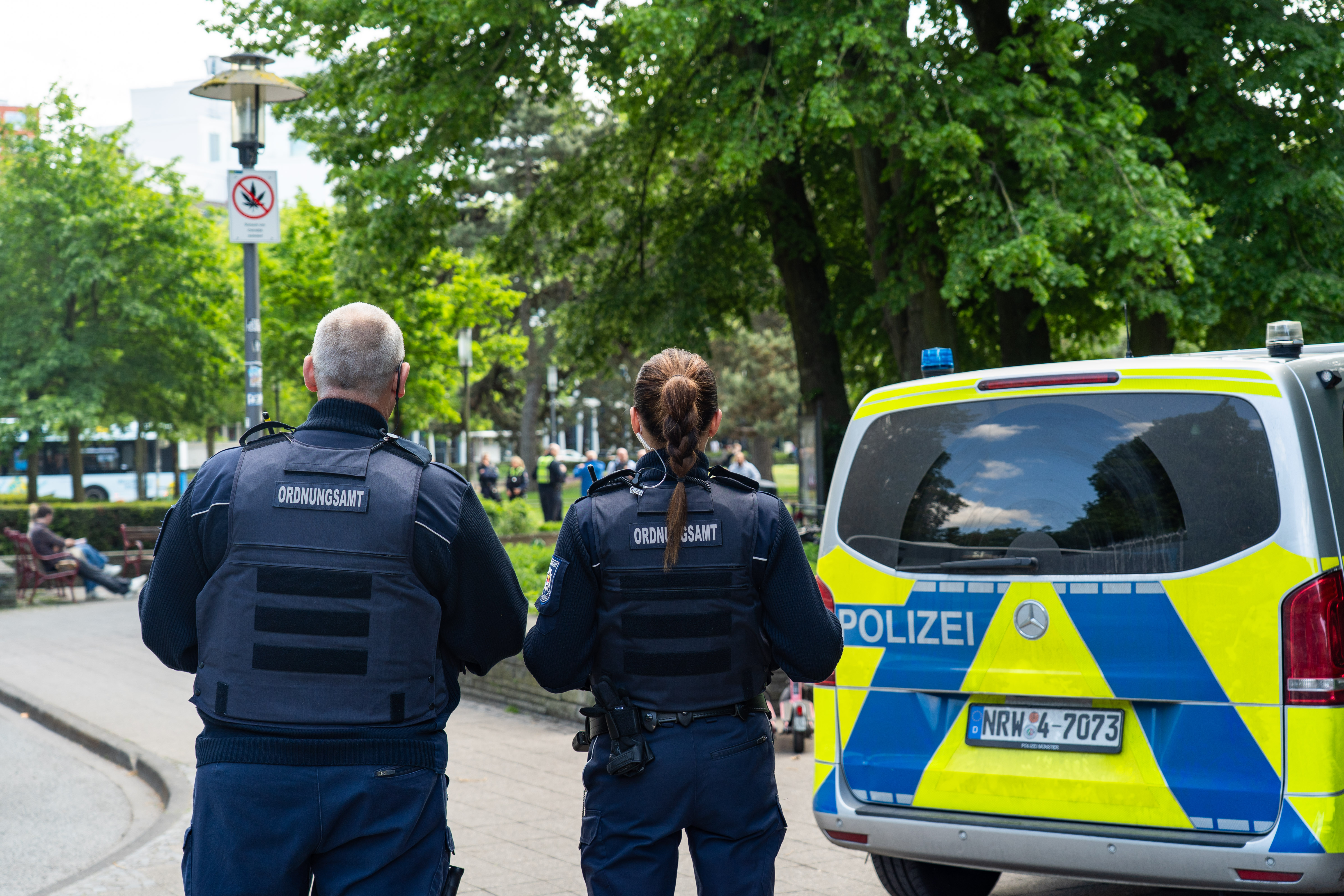 Mitarbeitende des Ordnungsamts vor Polizeiauto und Cannabisverbotsschild