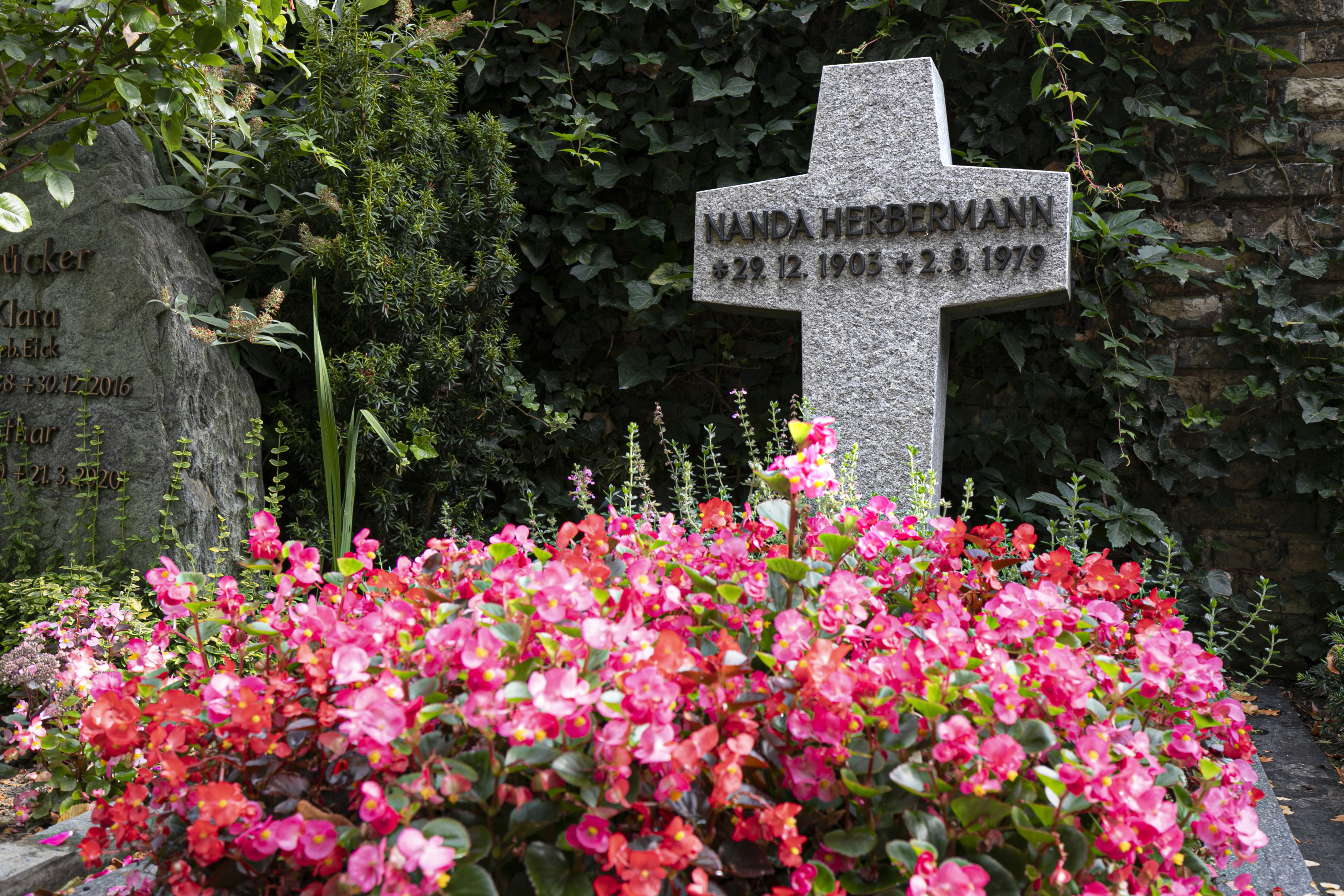 Ein Friedhofskreuz, davor rosarote Blumenpracht.