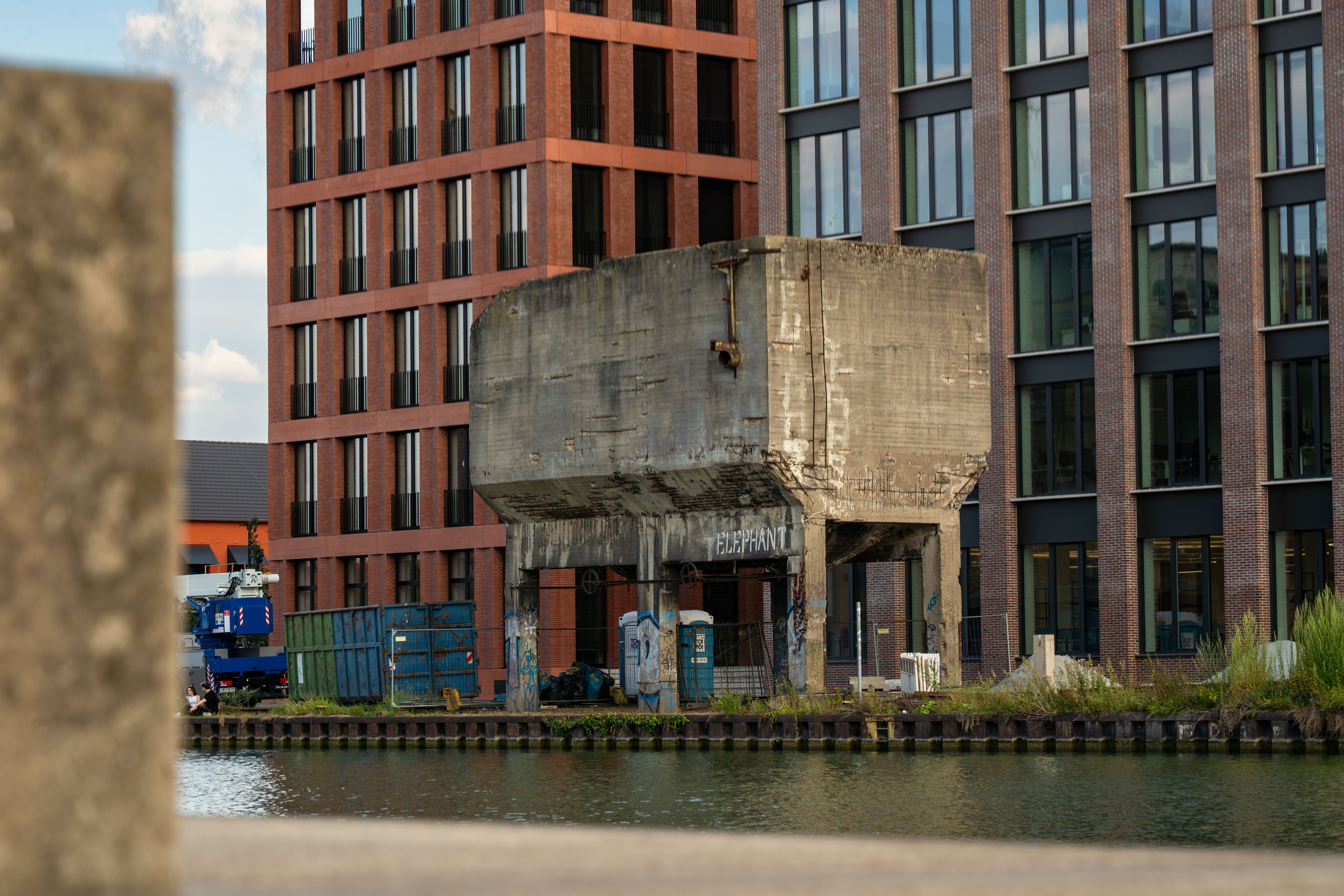 Blick über das Hafenbecken hin zum grauen Betonsilo, das auf vier grauen Säulen steht. Dahinter zwei mehrstöckige Bürogebäude, die das Silo überragen, mit großen und vielen Fenstern.