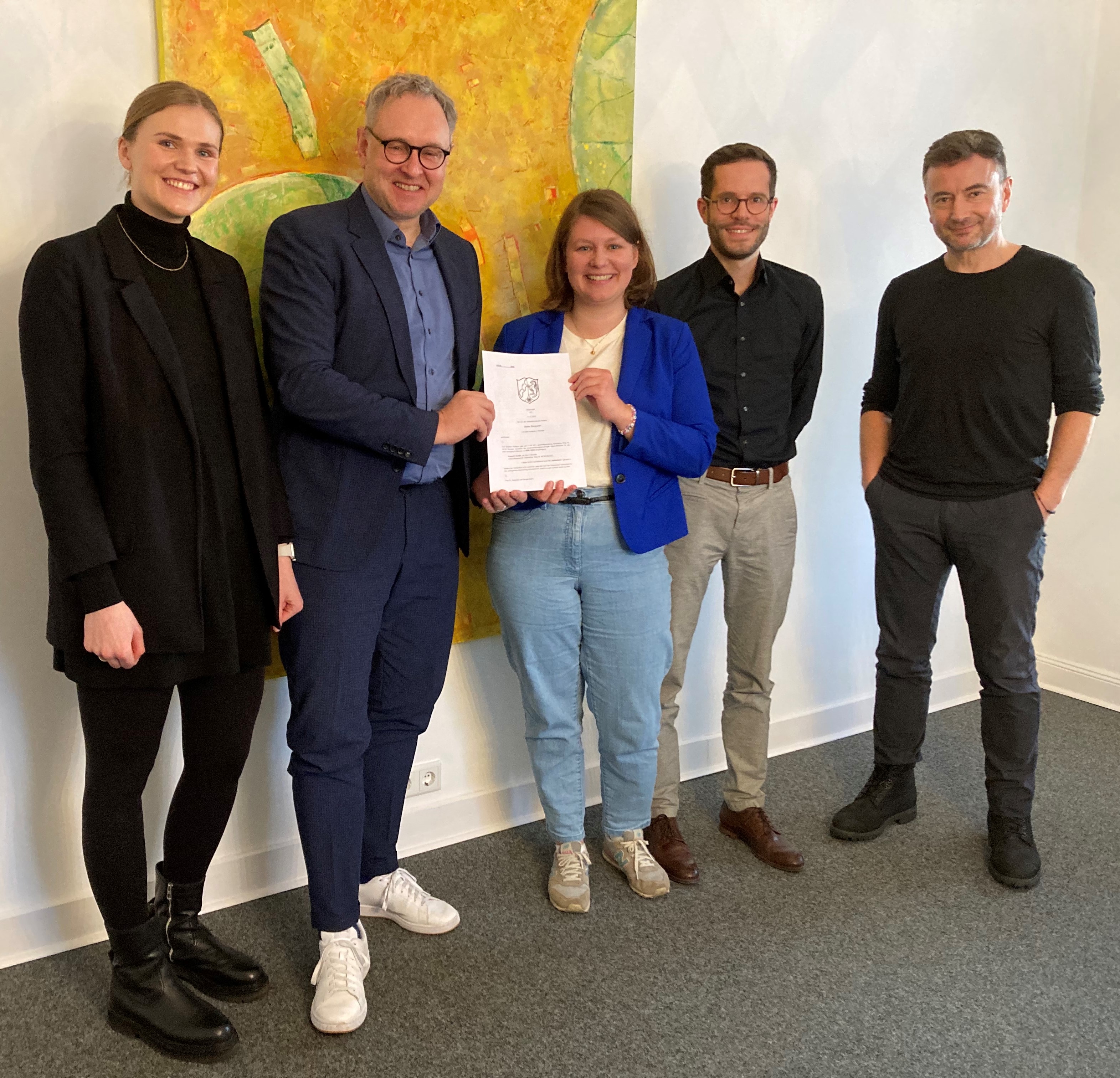 Fünf Menschen lächeln in die Kamera, zwei halten gemeinsam eine Urkunde