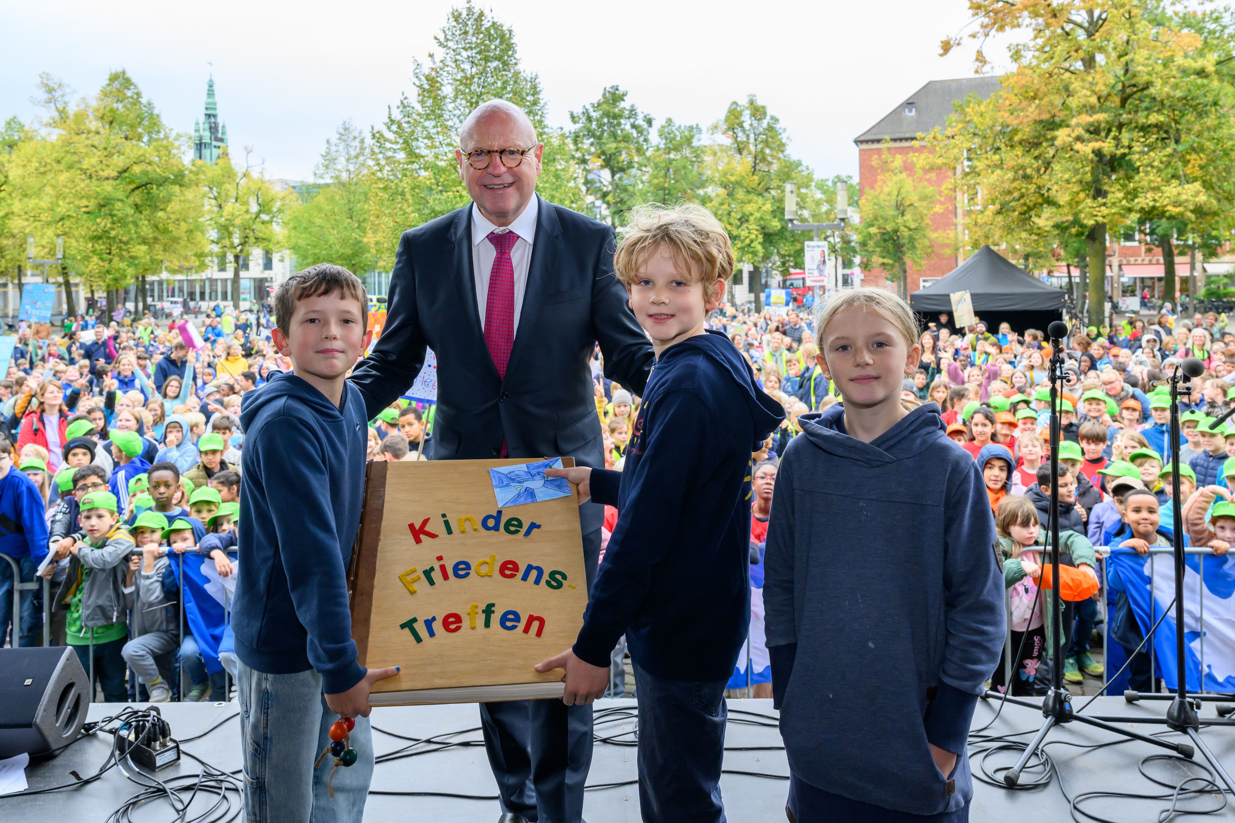 Oberbürgermeister Markus Lewe zusammen mit Teilnehmenden des Kinder-Friedensfests. Kinder überreichen ihm das Friedensbuch.  