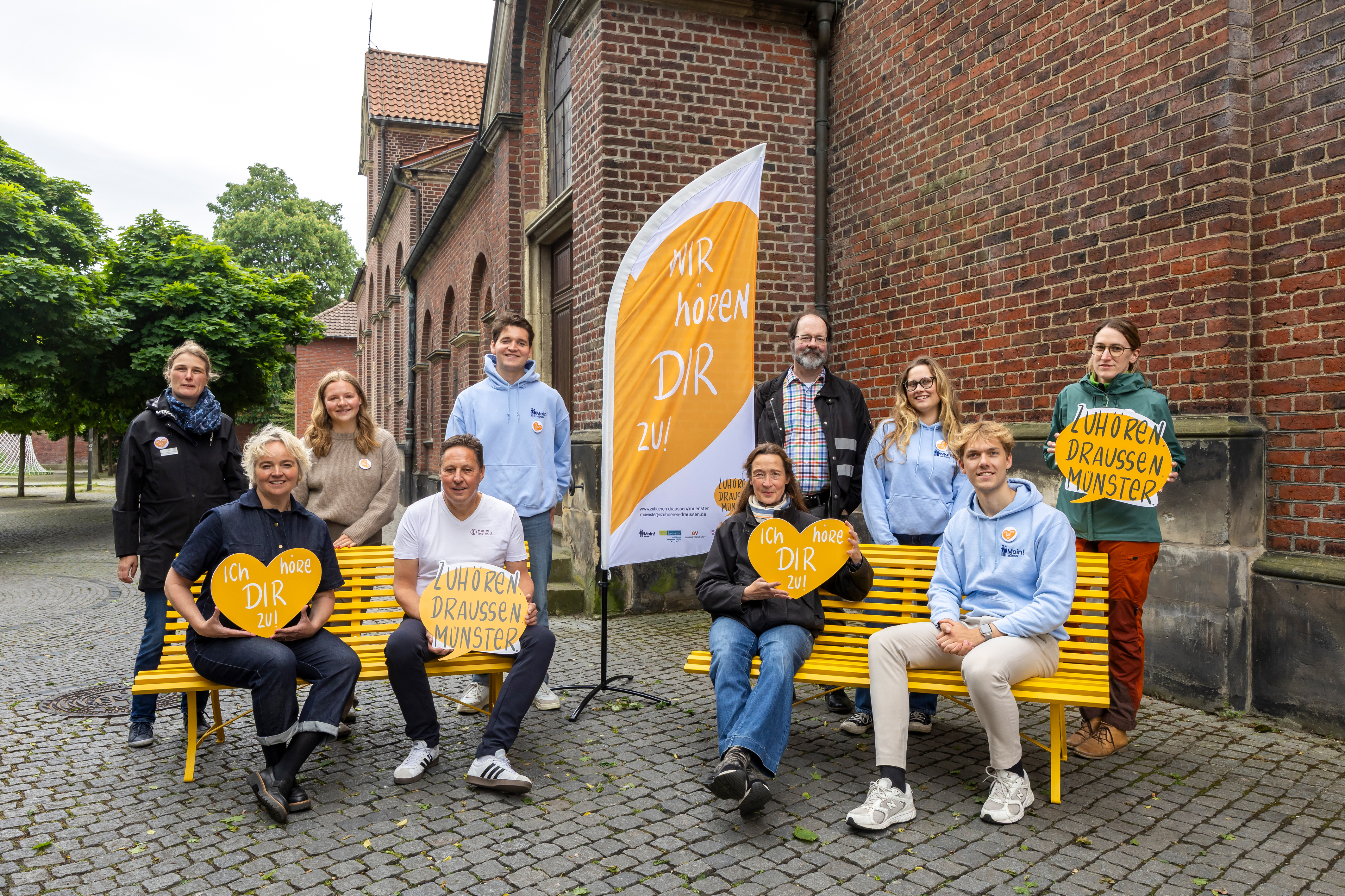 Das 10-köpfige Team von Zuhören.Draussen. Einige sitzen auf der Bank, andere stehen daneben.
