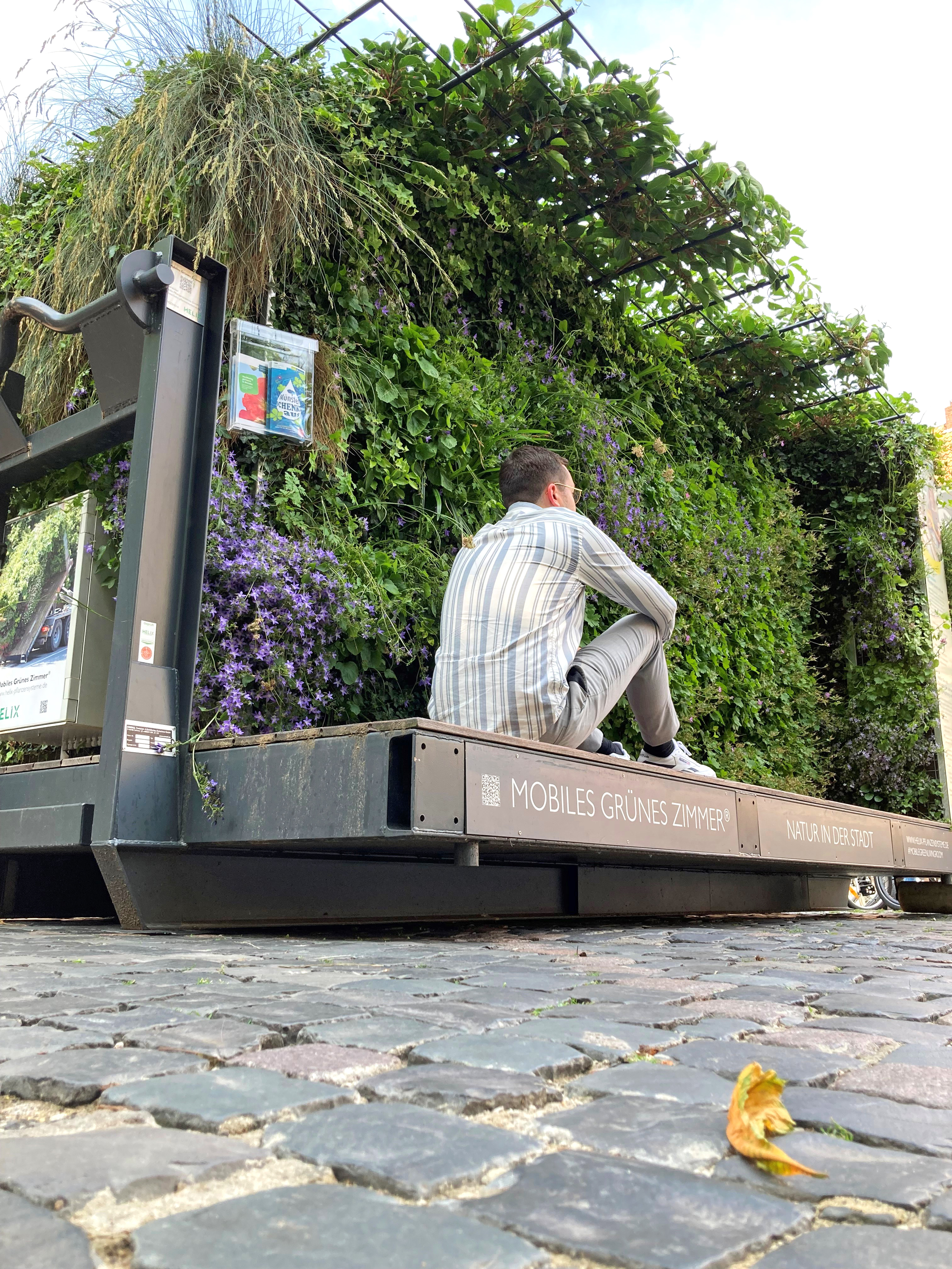 Man der auf einer Erhöhung sitzt, im Hintergrund ein begrüntes, mobiles Zimmer