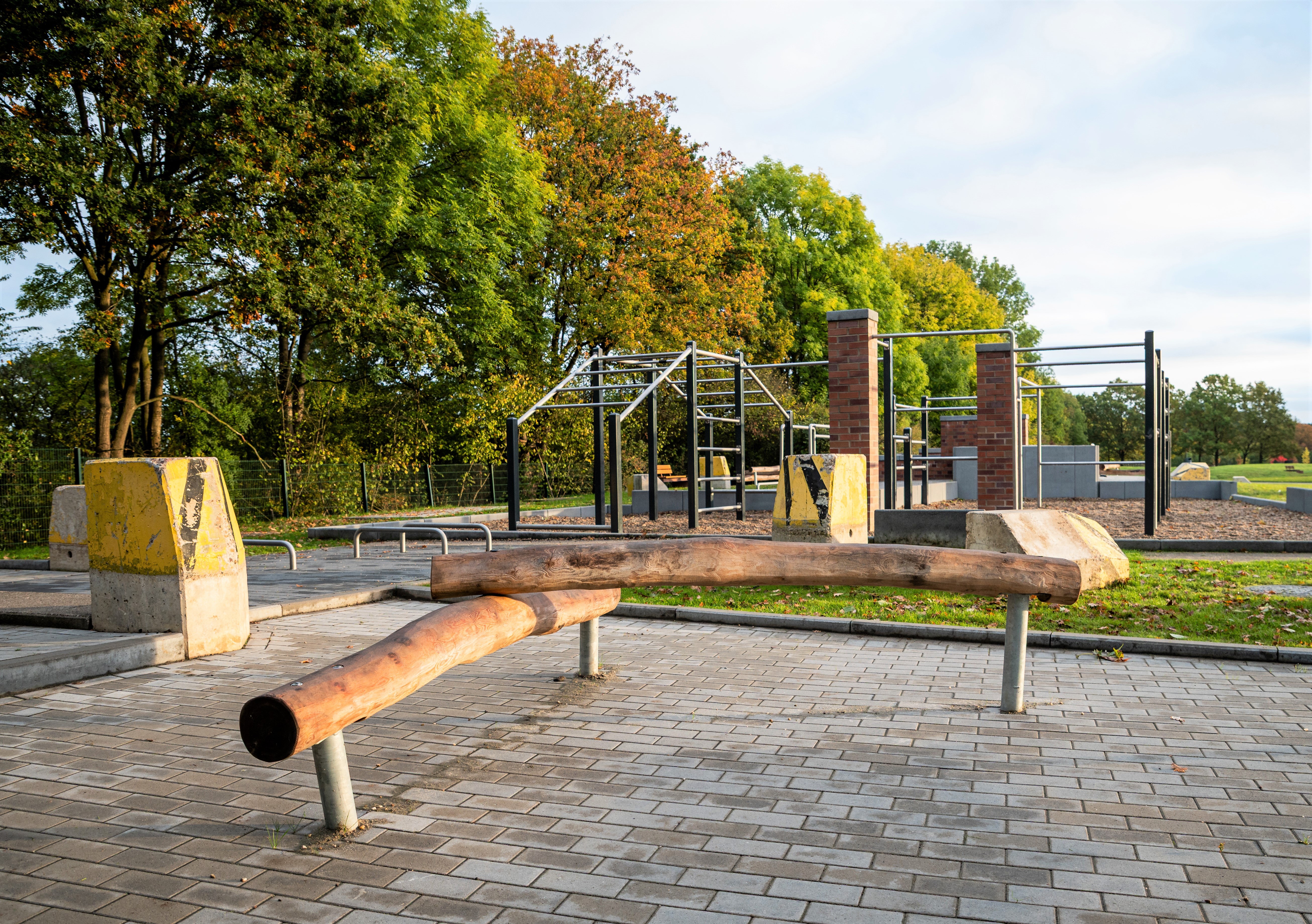 Parkour-Anlage aus Baumstämmen und Metallstangen vor Baumreihe