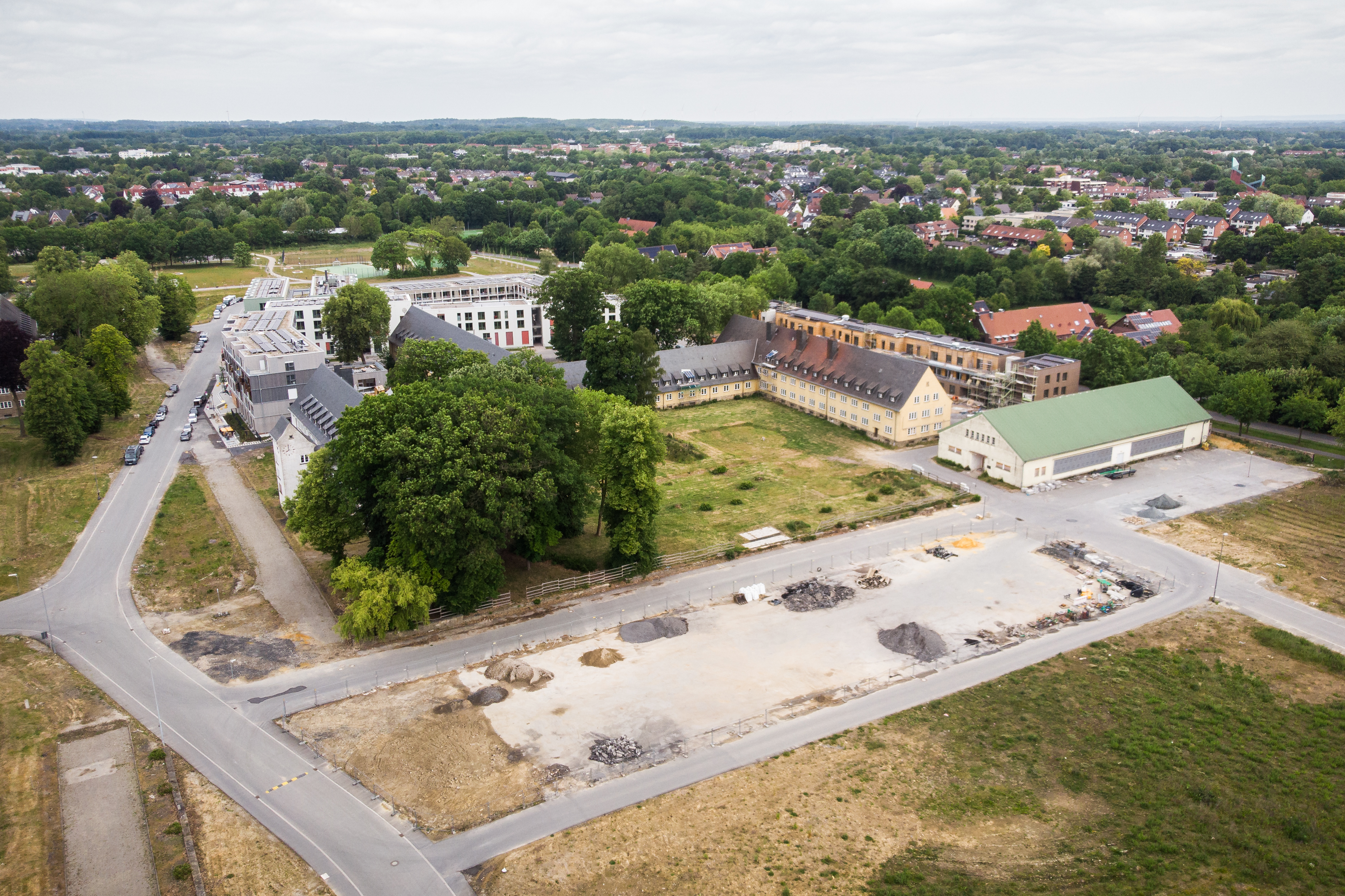 Luftbild des Areals, am Horizont erstreckt der Westen der Stadt. Im Vordergrund leere Flächen, auf denen anscheinend schon Arbeiten stattgefunden haben. Im Zentrum des Bildes sind die noch stehenden Gebäude.