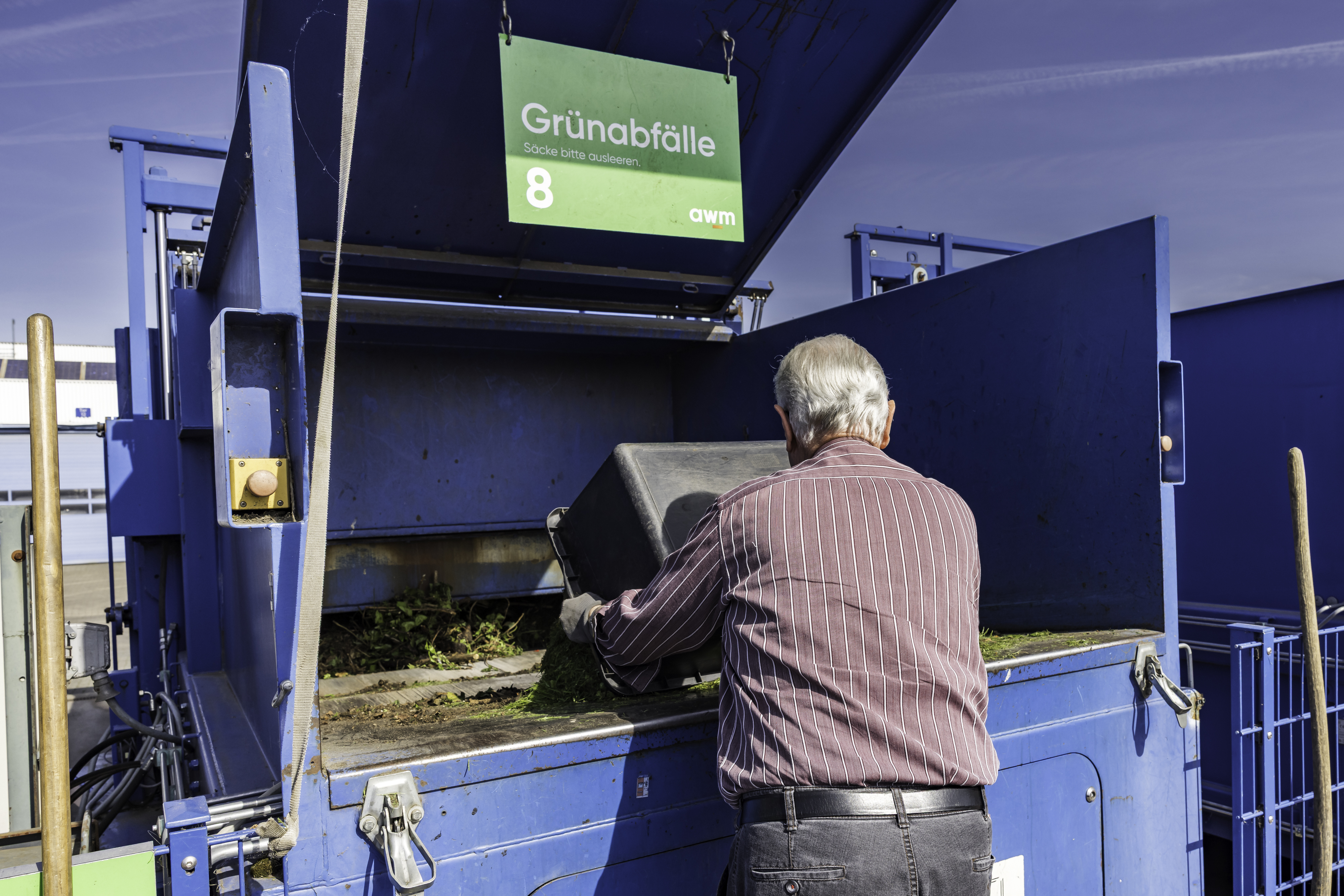 Eine Person steht vor einem Müllcontainer und wirft etwas hinein.