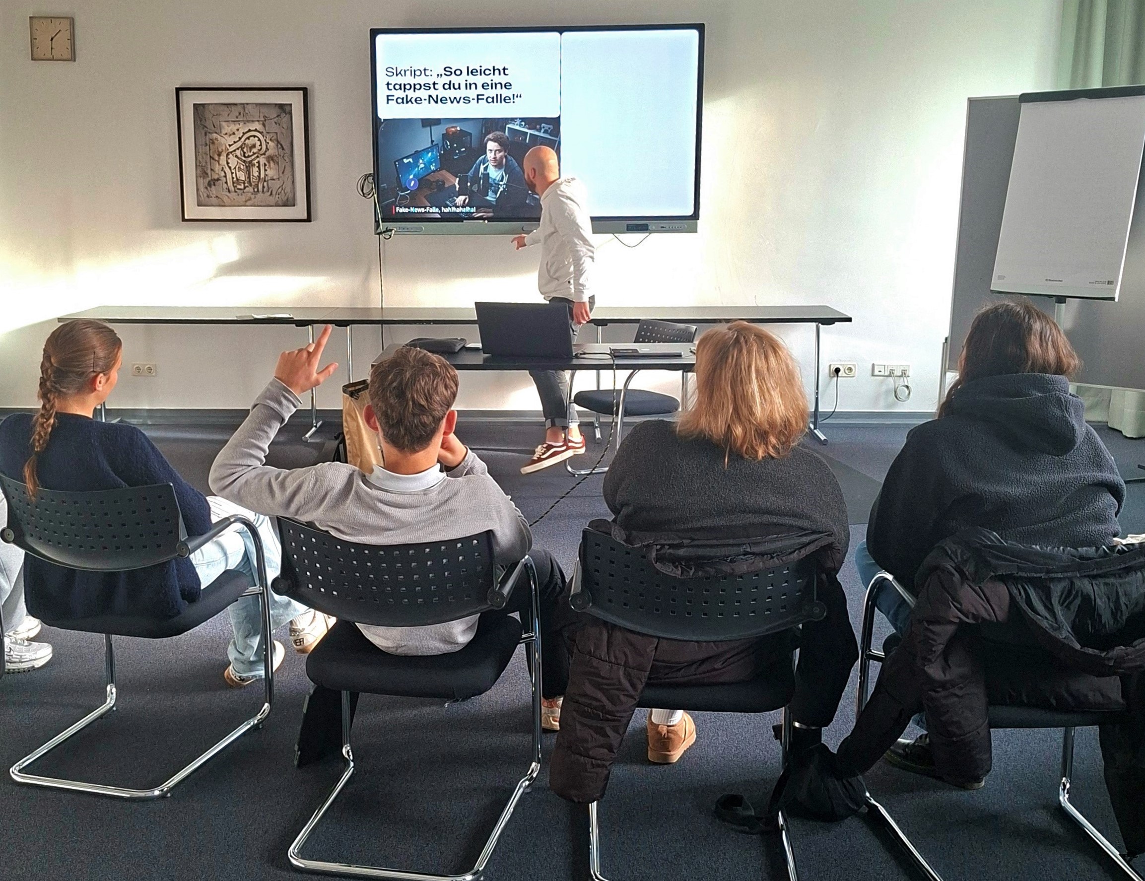 Ein Mann präsentiert ein Thema an einem Smartboard einer Gruppe von Schülerinnen und Schülern