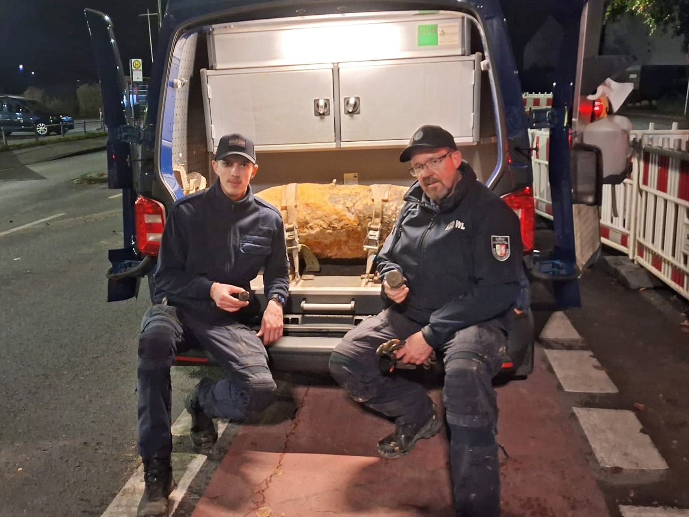 Zwei Männer knien vor einem Blindgänger, der im Kofferraum eines Autos liegt