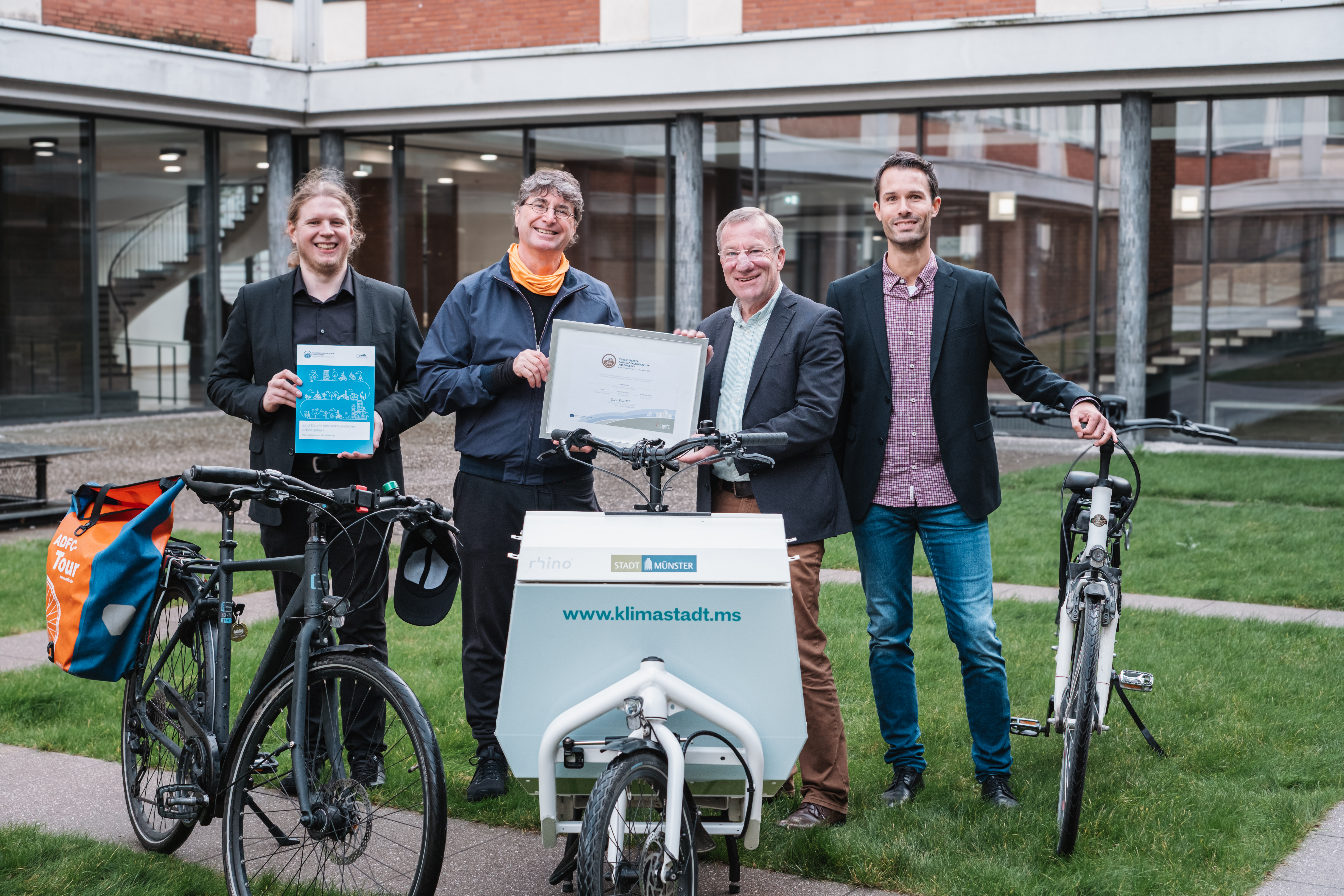Vier Männer stehen neben zwei Fahrrädern und einem Lastenrad und halten Dokumente in die Kamera.