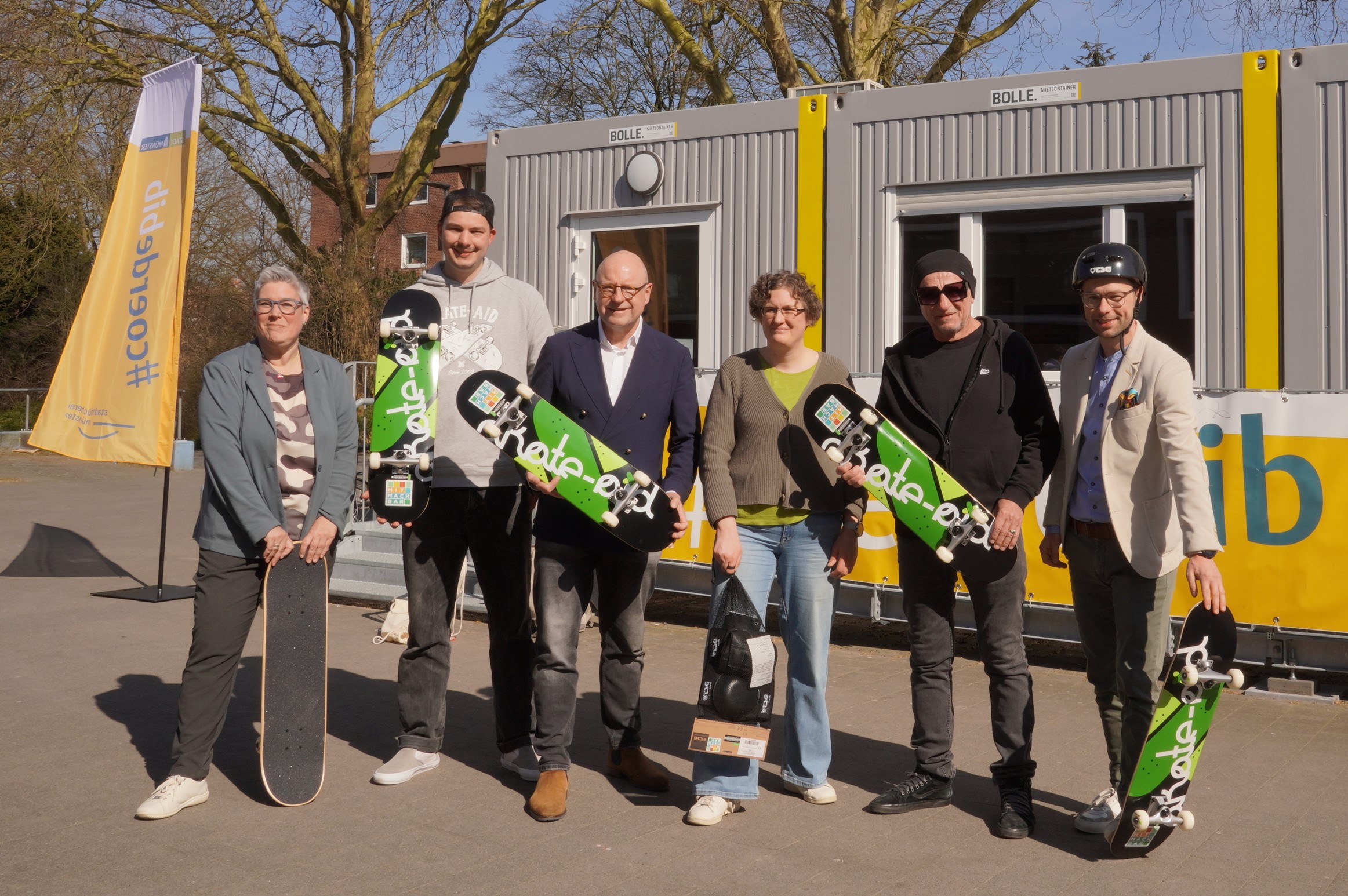 Cordula Gladrow, Leiterin der Stadtbücherei, Henning Timmes (skate-aid international e.V.), Oberbürgermeister Markus Lewe, Valja Schmitz (Stadtteilbücherei Coerde), Titus Dittmann (skate-aid international e.V.) und Christoph Mangelmans von der Josef Fiege Stiftung stehen aufgereiht jeweils mit Skateboards in den Händen.