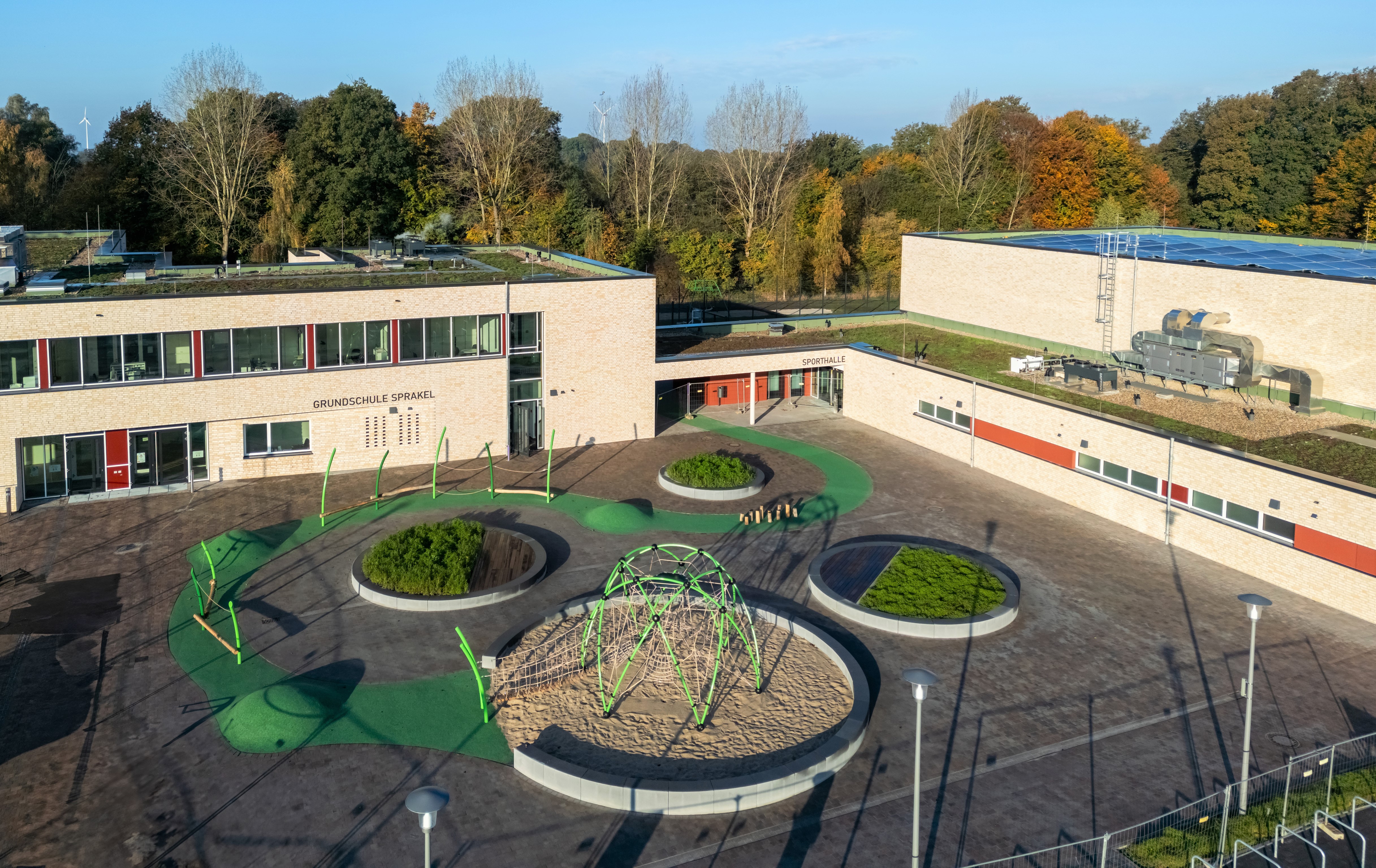 Ansicht der Grundschule von einem erhöhten Punkt. Im Mittelpunkt ist der von Schulgebäuden umgebene Schulhof mit runden Beeten.
