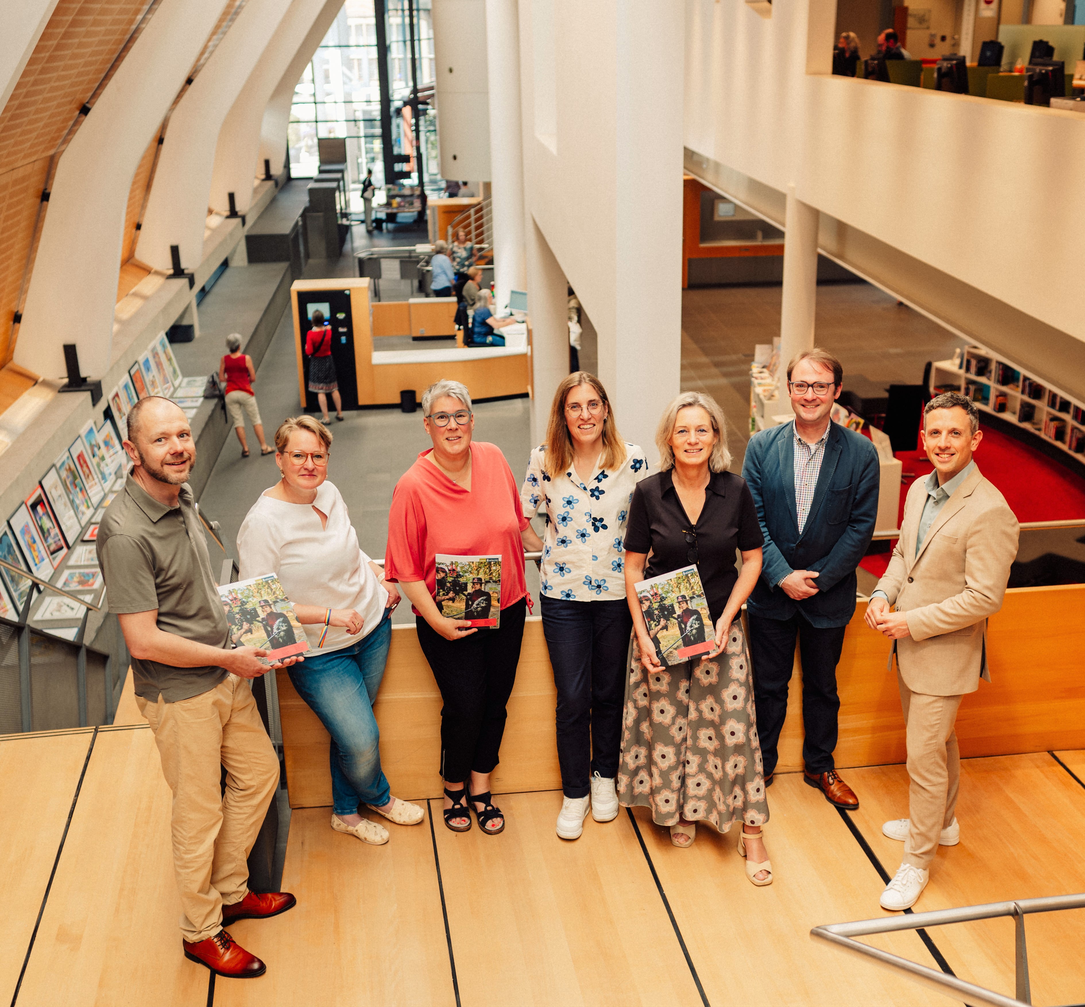 Auf einem Treppenabsatz in der Stadtbücherei stehen sieben Personen, manche halten das Kulturmagazin in den Händen.